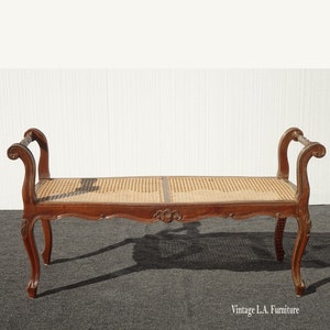 May include: A vintage wooden bench with a woven cane seat and scrolled arms. The bench has a dark brown finish and ornate carvings on the legs and arms.