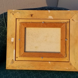 May include: A wooden picture frame with a light brown finish. The frame has a double border and is slightly distressed. The frame is empty and ready for a picture.