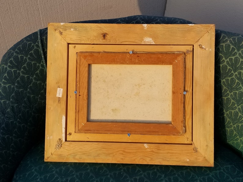 May include: A wooden picture frame with a light brown finish. The frame has a double border and is slightly distressed. The frame is empty and ready for a picture.