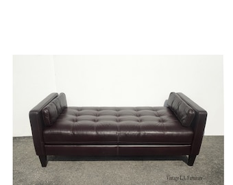 May include: A dark brown leather tufted daybed with two pillows. The daybed has a simple design with a rectangular shape and wooden legs.