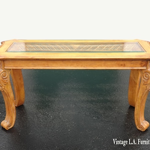 May include: A rectangular wooden coffee table with a glass top and ornate carved legs. The table has a light wood finish and the glass top is clear.