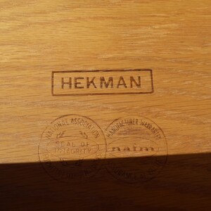 Może przedstawiać: Zbliżenie na drewnianą powierzchnię z trzema stemplami. G&oacute;rny stempel głosi "HEKMAN". Dolny lewy stempel głosi "National Association Seal of Integrity", a dolny prawy stempel głosi "Manufacturer Warranted nafm".