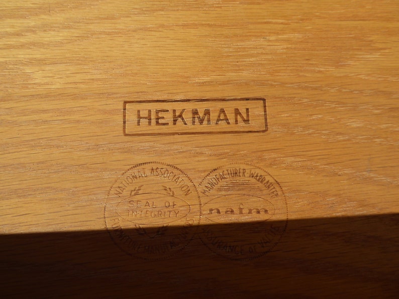 Może przedstawiać: Zbliżenie na drewnianą powierzchnię z trzema stemplami. G&oacute;rny stempel głosi "HEKMAN". Dolny lewy stempel głosi "National Association Seal of Integrity", a dolny prawy stempel głosi "Manufacturer Warranted nafm".
