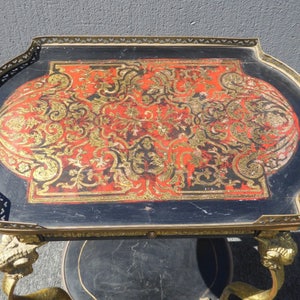 May include: A vintage brass and black serving cart with a red and gold patterned top. The cart has ornate lion paw feet and a decorative brass trim.