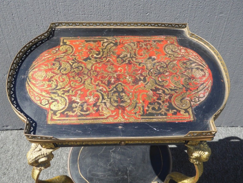May include: A vintage brass and black serving cart with a red and gold patterned top. The cart has ornate lion paw feet and a decorative brass trim.