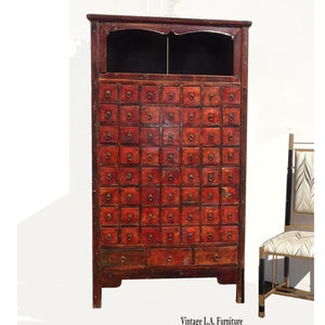 Op de afbeelding: Een vintage rode Chinese apothekerskast met een donkerhouten bovenblad en veel kleine laden. De kast heeft een verweerde uitstraling en is gemaakt van hout.
