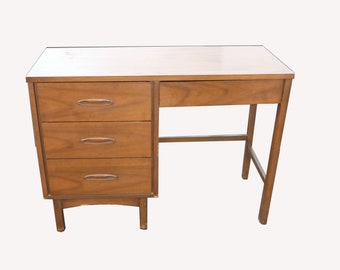 May include: A mid-century modern wooden desk with three drawers and a simple design. The desk is made of light brown wood and has a rectangular top.
