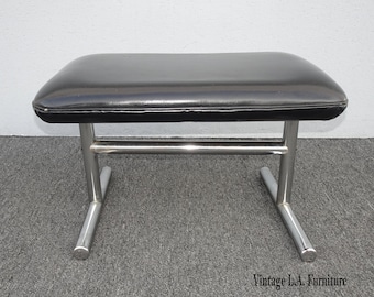May include: A black leather upholstered footstool with a chrome metal frame. The footstool has a simple, modern design.
