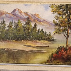May include: A painting of a mountain landscape with a lake in the foreground. The mountains are in the background and are covered in snow. There are trees in the foreground and a small lake in the middle of the painting. The painting is signed "E. Strawn" in the bottom left corner.