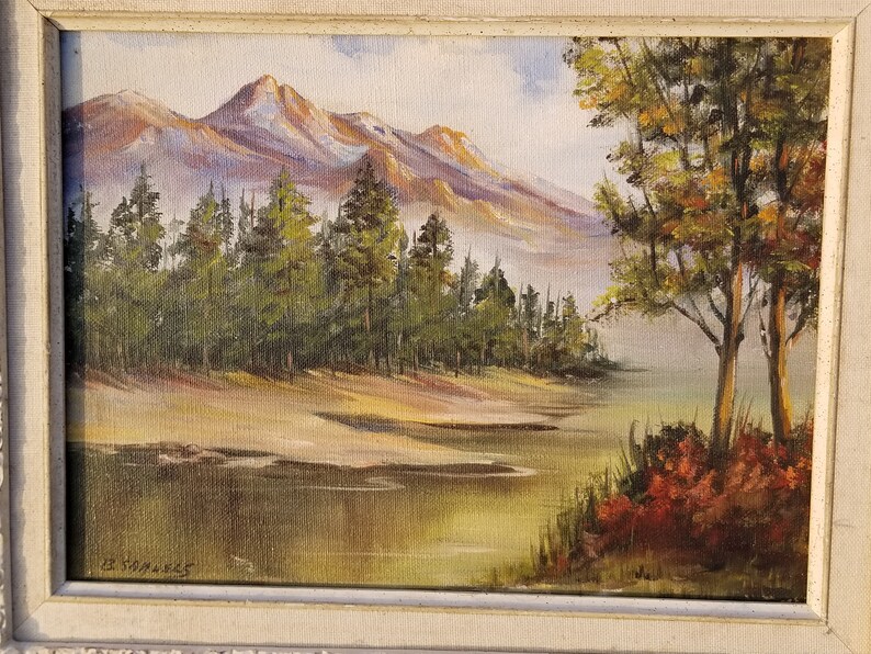May include: A painting of a mountain landscape with a lake in the foreground. The mountains are in the background and are covered in snow. There are trees in the foreground and a small lake in the middle of the painting. The painting is signed "E. Strawn" in the bottom left corner.
