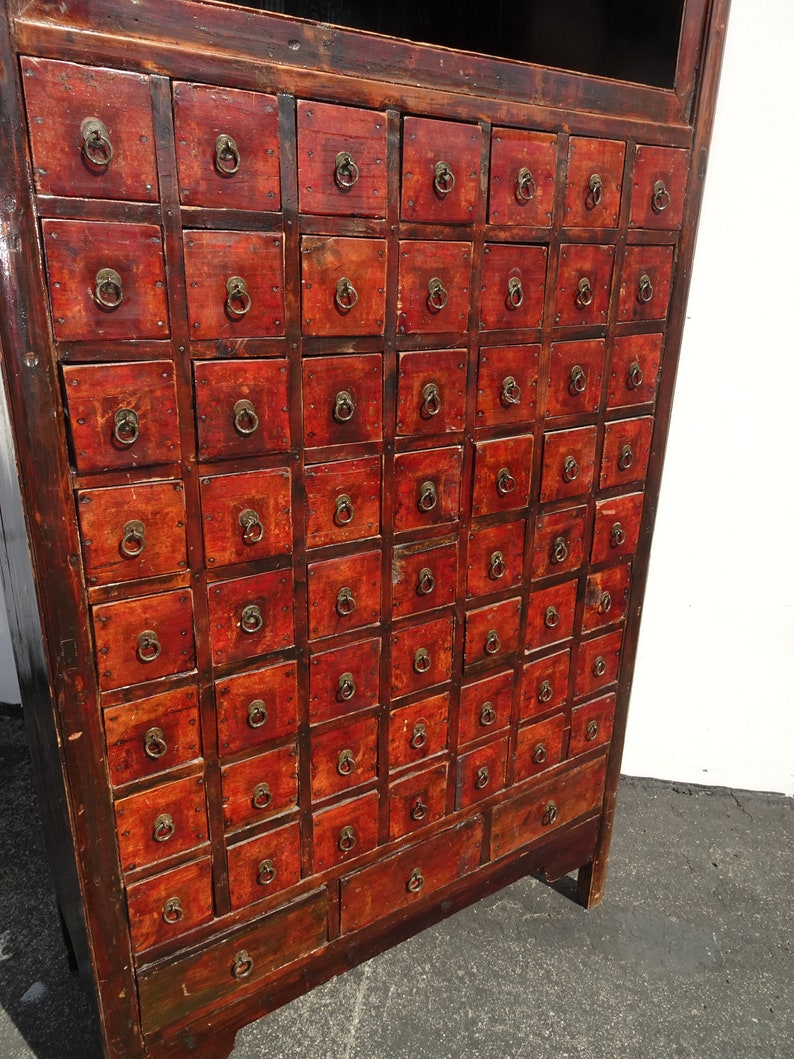 Op de afbeelding: Antiek Chinees apothekerskast met meerdere kleine laden, elk met een messing ringgreep. De kast is gemaakt van donker hout met een roodbruine afwerking en heeft een verweerde uitstraling.