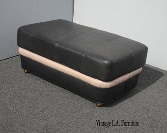 May include: A black leather ottoman with a pink leather trim. The ottoman has a tufted top and sits on four legs.