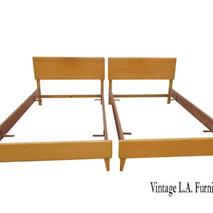May include: Two wooden bed frames with headboards. The frames are made of light-colored wood and have a simple, mid-century modern design. The headboards are rectangular and the legs are tapered.