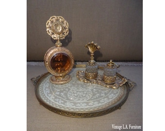 May include: A gold-toned tray with a lace design on the bottom. The tray holds three glass perfume bottles with ornate gold tops.