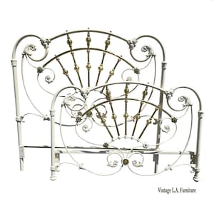 May include: A vintage white metal bed frame with brass accents. The headboard and footboard feature ornate scrollwork and floral details. The bed frame is a classic design, perfect for a bedroom. The text "Vintage L.A. Furniture" is at the bottom.