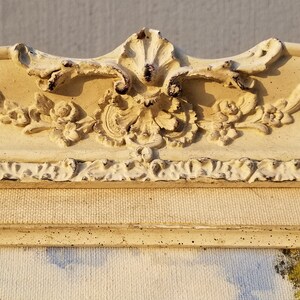 May include: A close-up of a white, ornate picture frame with a distressed finish. The frame has a raised, floral design and a textured surface.
