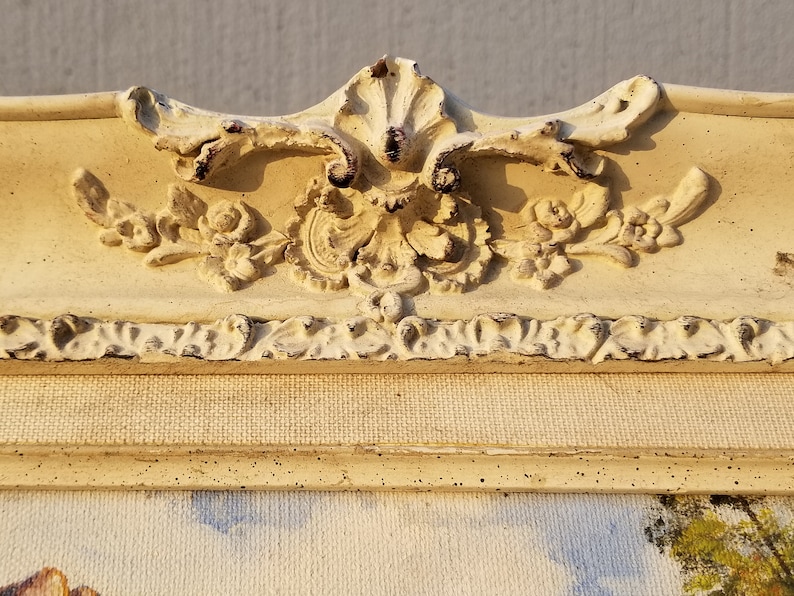 May include: A close-up of a white, ornate picture frame with a distressed finish. The frame has a raised, floral design and a textured surface.