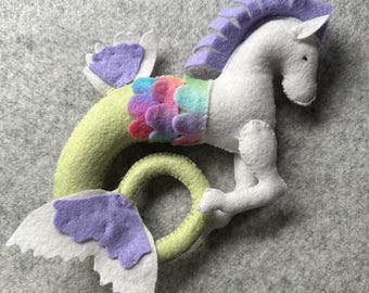 Könnte beinhalten: Ein handgefertigtes Filz-Seepferdchen-Spielzeug mit einer lila-weißen Mähne, einem regenbogenfarbenen Schwanz und einer grün-weißen Schwanzflosse.