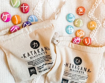 May include: Two white canvas bags with colorful magnetic letters spelling out the Japanese words "Katakana" and "Hiragana". The bags contain 46 magnetic letters each, and the text on the bags describes the Japanese writing systems.