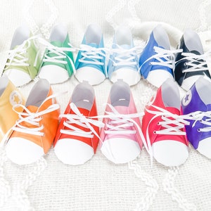May include: A set of ten paper baby shoes in various colors, including green, blue, yellow, orange, red, pink, purple, and black. The shoes are decorated with white laces and a white sole.