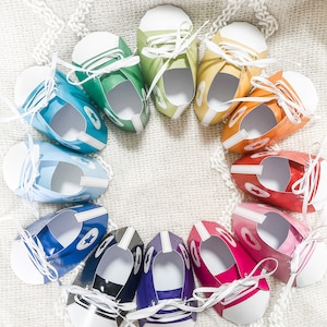 May include: A circle of colorful paper shoes with white laces. The shoes are arranged in a rainbow pattern, starting with green and ending with red.