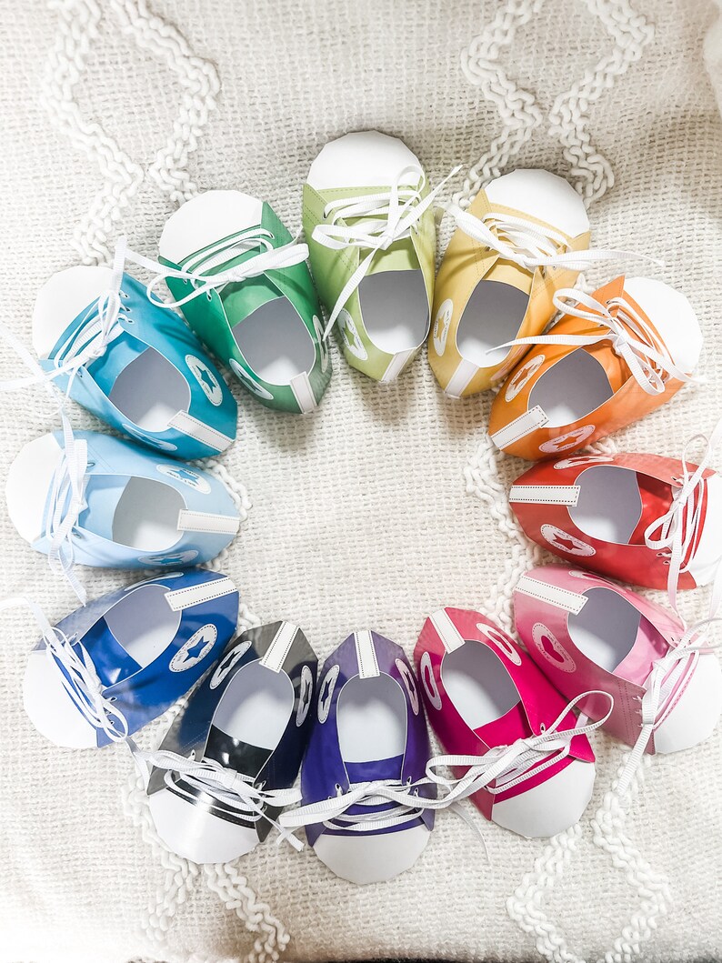 May include: A circle of colorful paper shoes with white laces. The shoes are arranged in a rainbow pattern, starting with green and ending with red.
