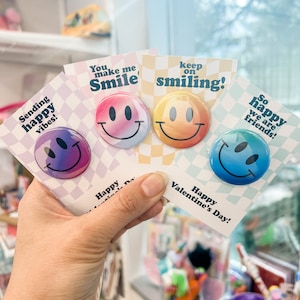 May include: Four colorful smiley face buttons with different messages on each. The messages are "Sending happy vibes!" "You make me smile" "Keep on smiling!" and "So happy we are friends!"