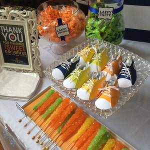 May include: A table setting for a party with a variety of treats, including candy popcorn, Laffy Taffy, rock candy, and shoe-shaped favors. The table is decorated with a sign that says "Thank You for Sharing this Sweet Day with Us".