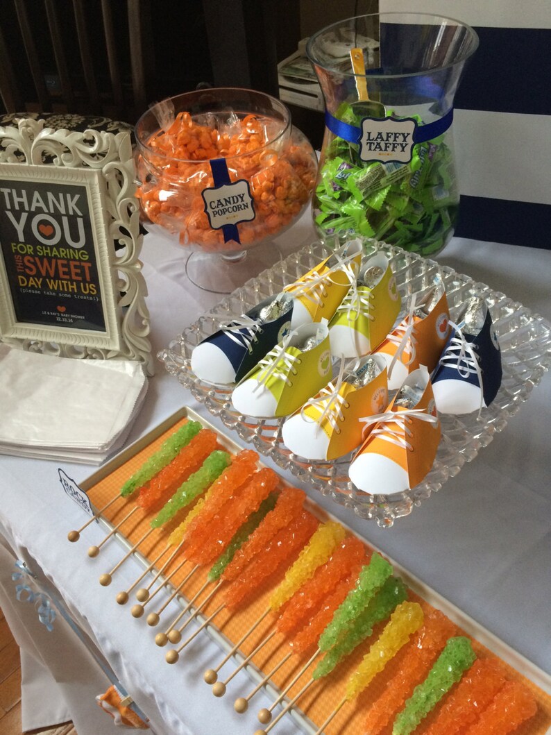 May include: A table setting for a party with a variety of treats, including candy popcorn, Laffy Taffy, rock candy, and shoe-shaped favors. The table is decorated with a sign that says "Thank You for Sharing this Sweet Day with Us".