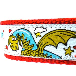May include: A red braided collar with a white ribbon featuring cartoon dragons, hearts, and stars. The dragons are yellow and blue, set against a light blue background. The collar is designed for pets.