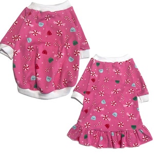May include: Two pink dog pajamas with a candy cane and peppermint pattern. One pajama is a long-sleeved shirt and the other is a dress with a ruffled hem.
