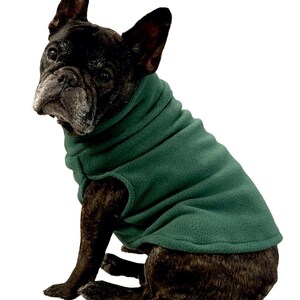 May include: A brindle French Bulldog wearing a dark green fleece dog sweater. The dog is sitting and looking towards the left. The sweater covers the dog's chest and back.