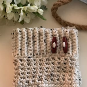 May include: Cream-colored crocheted leg warmers with a speckled pattern and two brown wooden buttons.