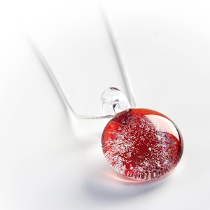 May include: A silver chain necklace with a red glass pendant. The pendant has a white speckled design and a clear glass bail.