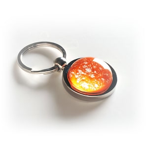 May include: A silver keychain with a round, orange and yellow glass charm. The glass charm has white flecks throughout.