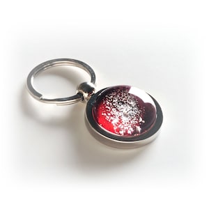 May include: A silver key chain with a round red glass charm. The glass charm has white flecks throughout.