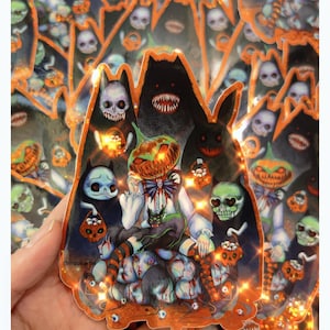 May include: A collection of Halloween-themed stickers featuring spooky illustrations. The stickers showcase a central figure with a pumpkin head, surrounded by skulls, monsters, and other eerie characters. The color palette includes orange, black, white, and touches of blue and green.