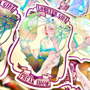 Könnte beinhalten: Ein gestanzter Aufkleber mit der Illustration einer Person mit Hummerkopfschmuck und einer großen Schere. Das Design hat einen violetten Rand, ein Banner oben mit der Aufschrift LOBSTER GIRL und ein Banner unten mit FREAK SHOW.