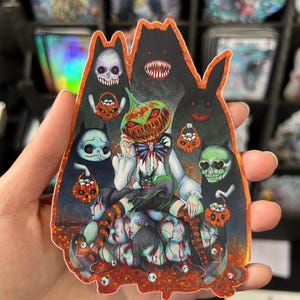 May include: A holographic sticker featuring a spooky Halloween-themed illustration. The artwork includes a pumpkin-headed figure, various monster silhouettes, and a pile of severed heads. The sticker has a glittery, iridescent finish.