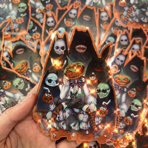 May include: A Halloween-themed sticker featuring a central illustration of a figure with a pumpkin head, surrounded by skulls, jack-o'-lanterns, and dark, shadowy figures. The sticker has a dark color palette with orange and white accents, creating a spooky aesthetic.
