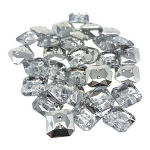 May include: A collection of clear, faceted, square-shaped glass beads with a reflective, metallic silver finish. Each bead has a small, silver-coloured stud in the centre. The beads are scattered against a white background.