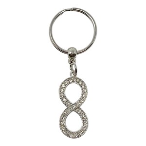 May include: Silver-coloured keyring featuring an infinity symbol pendant. The infinity symbol is adorned with small, clear crystals. The keyring has a round key ring and a small connector.