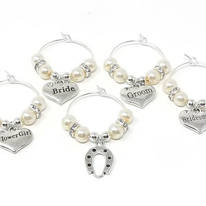 May include: Set of five silver-tone glass charms with white pearl beads. Each charm features a heart-shaped pendant with the words "Bride", "Groom", "Bridesmaid", "Flower Girl", and a horseshoe.