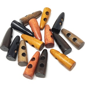May include: A collection of wooden toggle buttons in various colours, including black, brown, orange, and yellow. The buttons have two holes and a pointed tip.