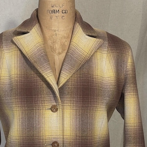 Puede incluir: Una chaqueta de cuadros marrones y amarillos con cierre de botones y dos bolsillos de solapa. La chaqueta tiene cuello y mangas largas.