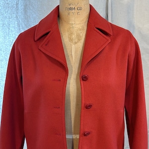 May include: A red wool jacket with a button fastening and a collar. The jacket has a simple design and is in good condition.