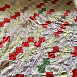 May include: A patchwork quilt with a repeating pattern of red, white, yellow, brown, green, and purple squares. The quilt is made of different fabrics and has a slightly wrinkled texture.
