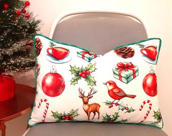 May include: A decorative pillow with a white background and a green border. The pillow features Christmas-themed illustrations, including red ornaments, gifts, holly, a deer, a bird, and candy canes.