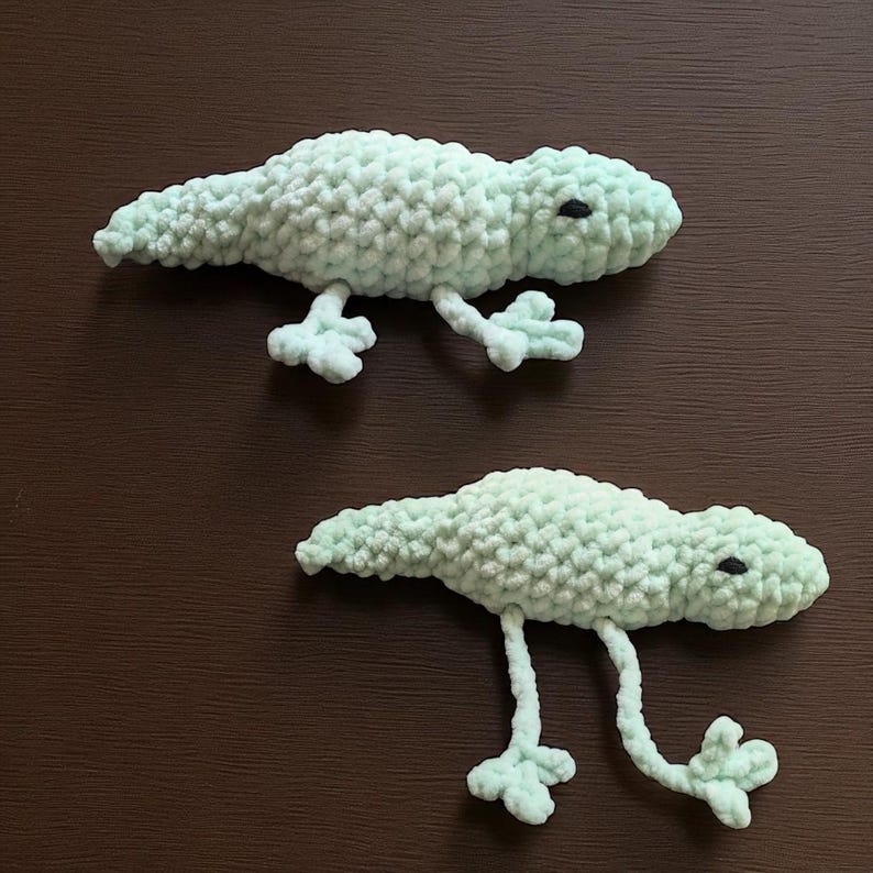 A crochet mint green lizard with arms and legs that can be pulled back and forth to create a quiet fidget.