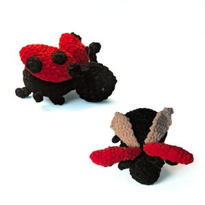 May include: Two crocheted plush toys shaped like insects. One is a ladybug with a black body and red wings featuring black spots. The other is a bee-like figure with a black body, one pair of red wings, and one pair of light beige wings.